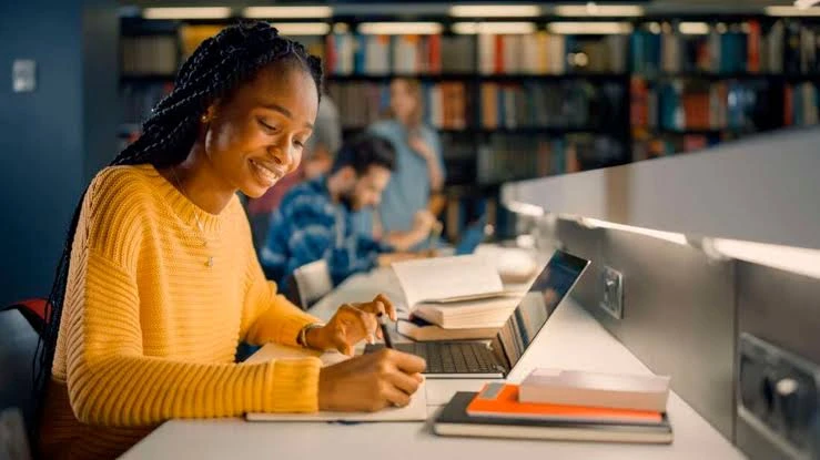 Kingdom Foundation College student smiling while studying with a laptop and notebook